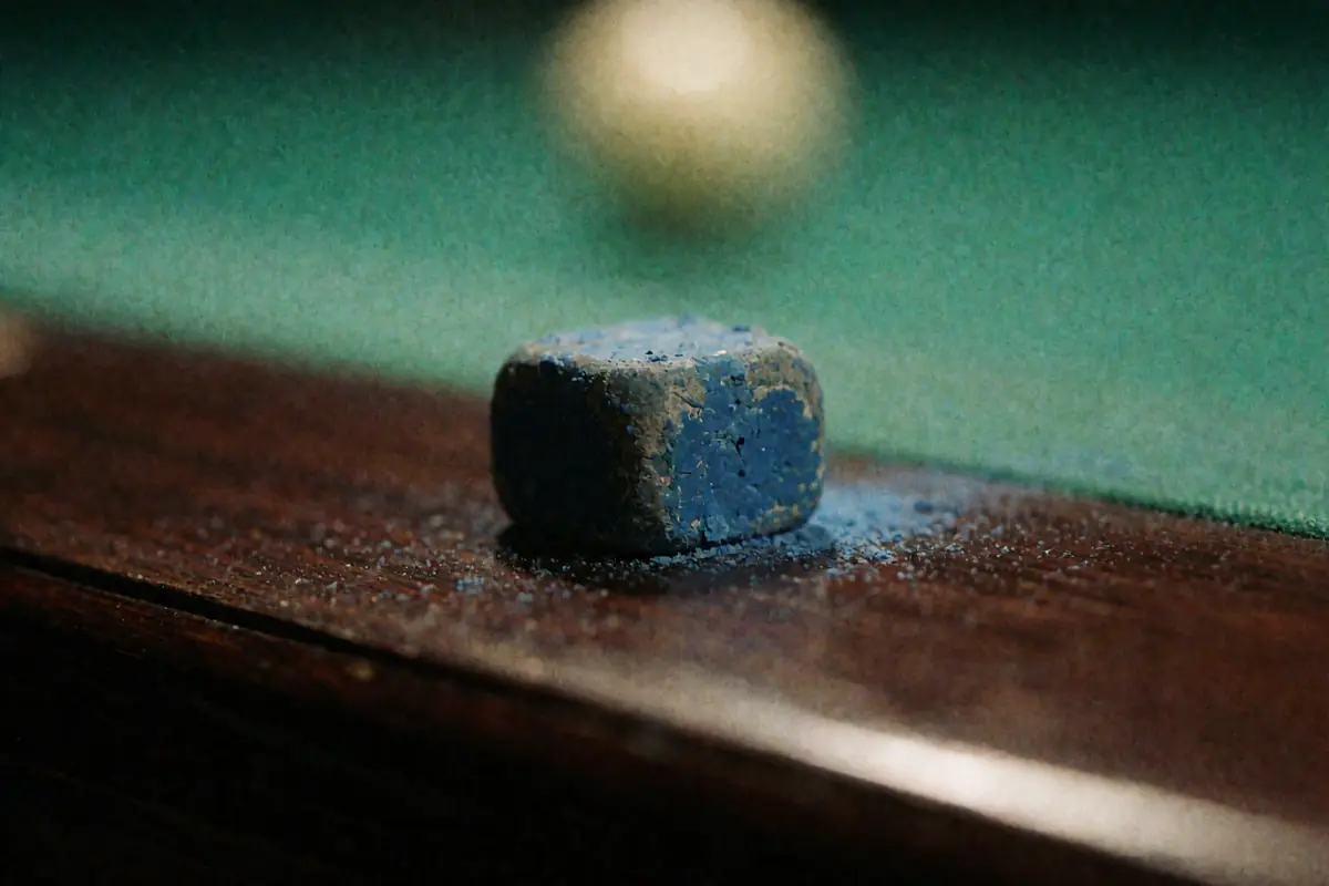 Un cubetto di gesso blu consumato appoggiato sulla sponda di legno del tavolo